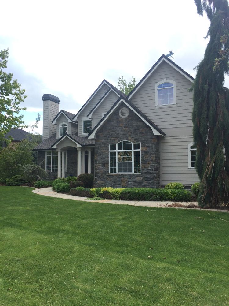 Two-story house with gray siding, stone accents, and manicured lawn.