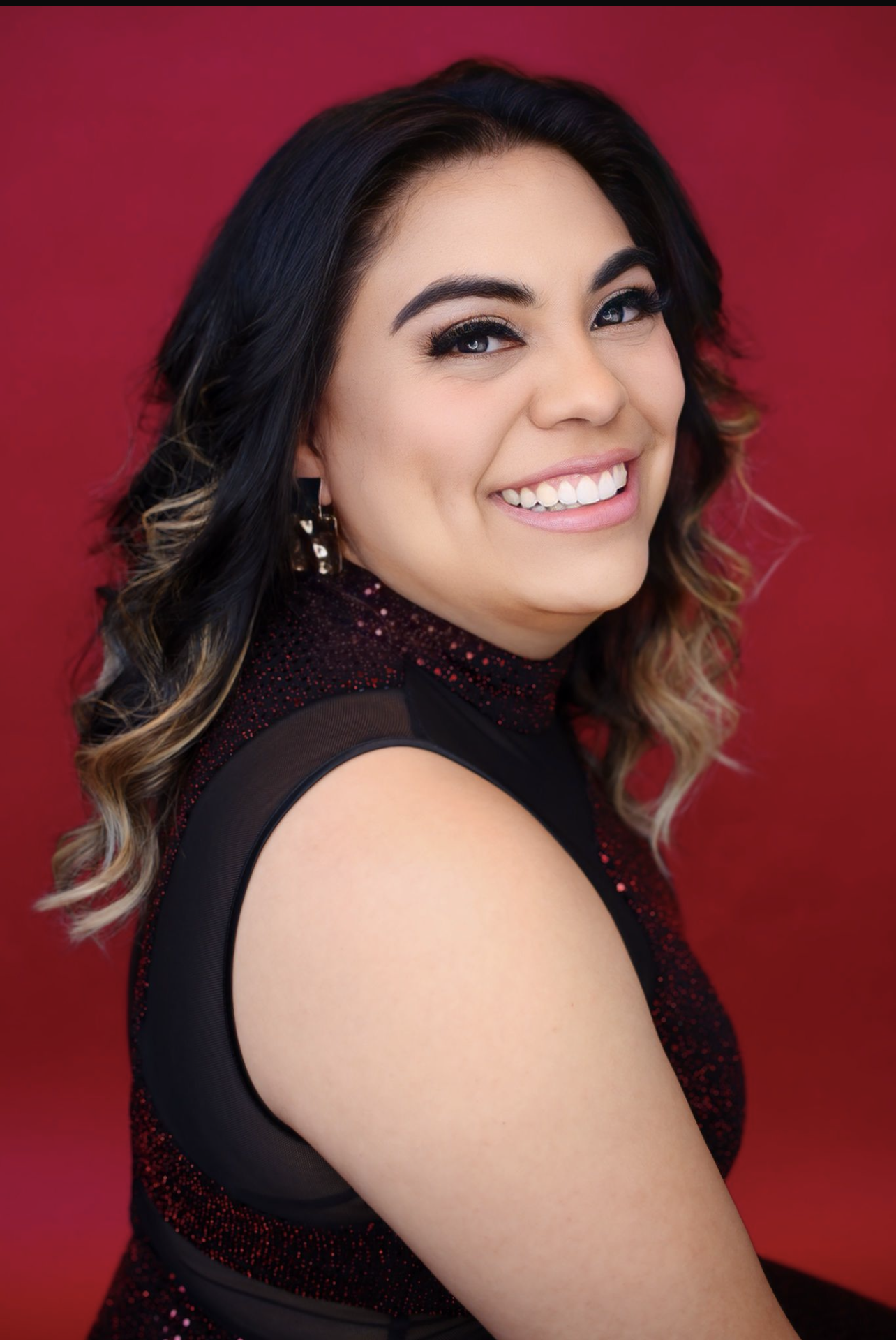 A woman in a black dress is smiling in front of a red background