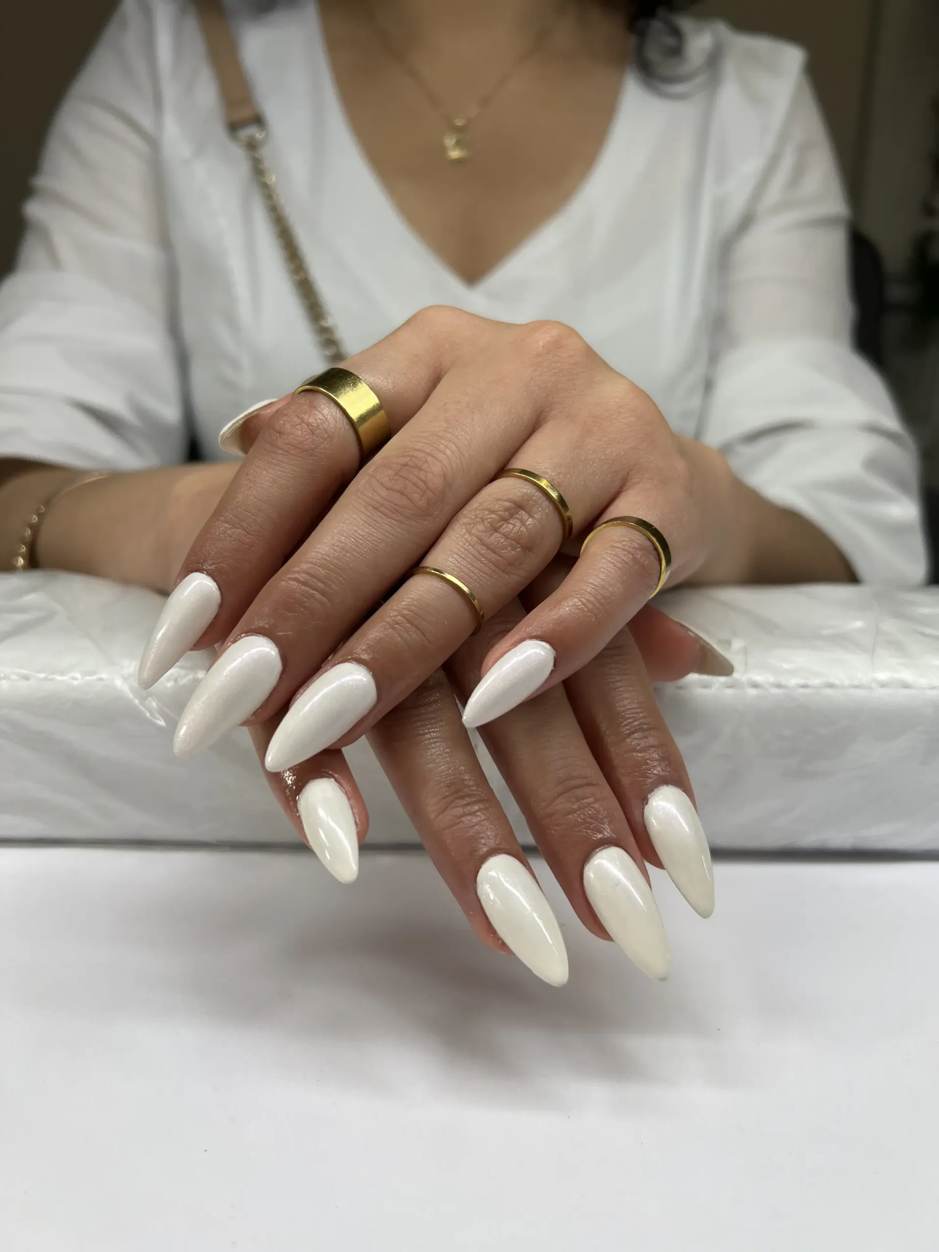A woman with long white nails and rings on her fingers is sitting at a table.