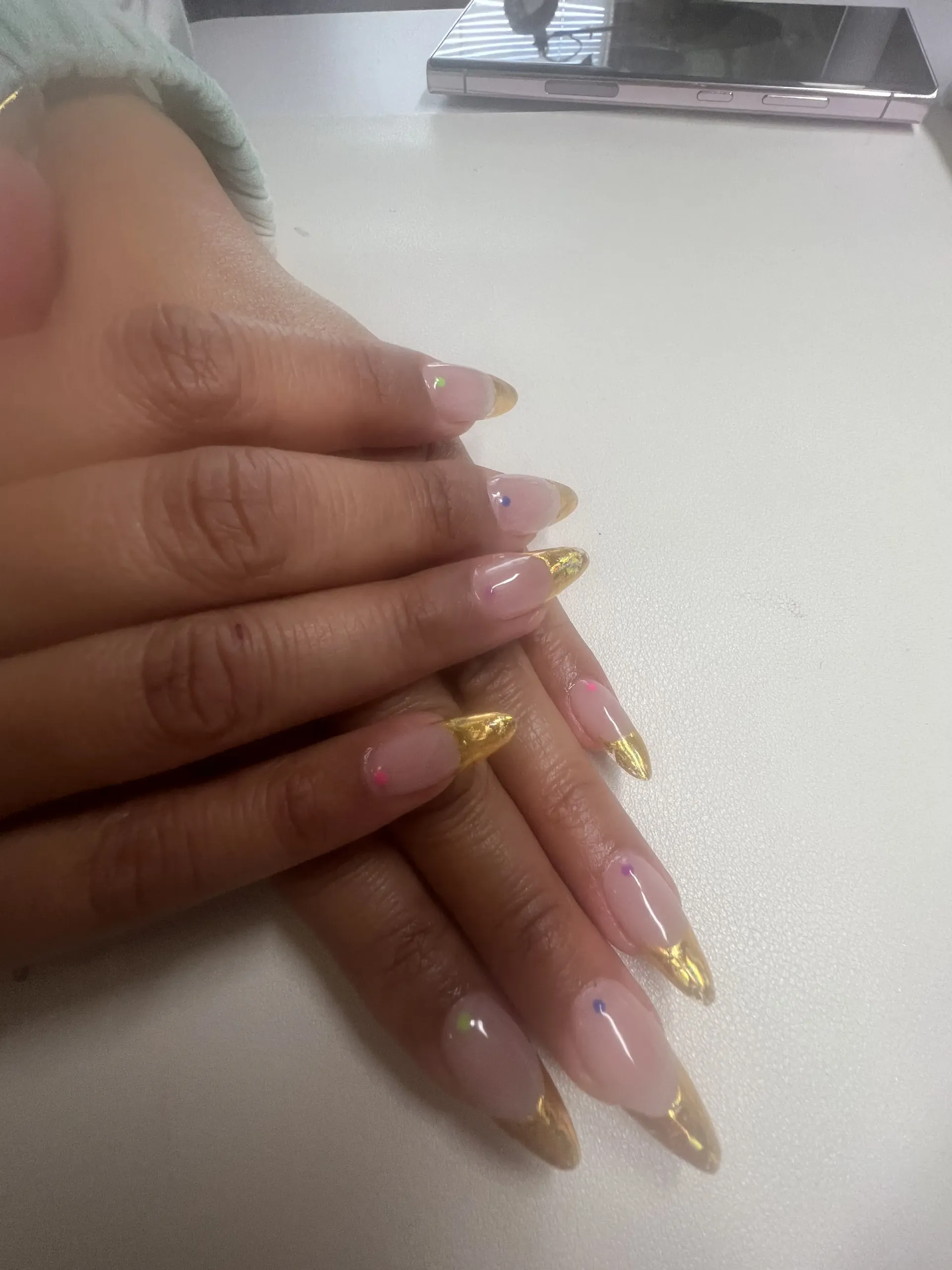 A close up of a person 's nails on a table with a phone in the background.