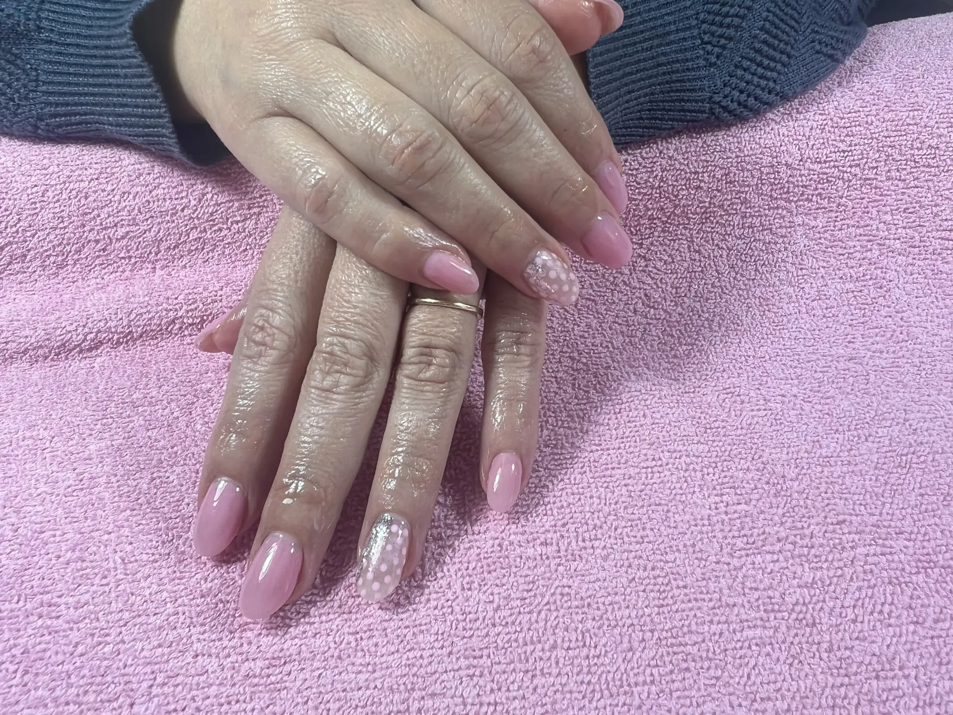 A woman 's hands with pink nails and a ring on a pink towel.