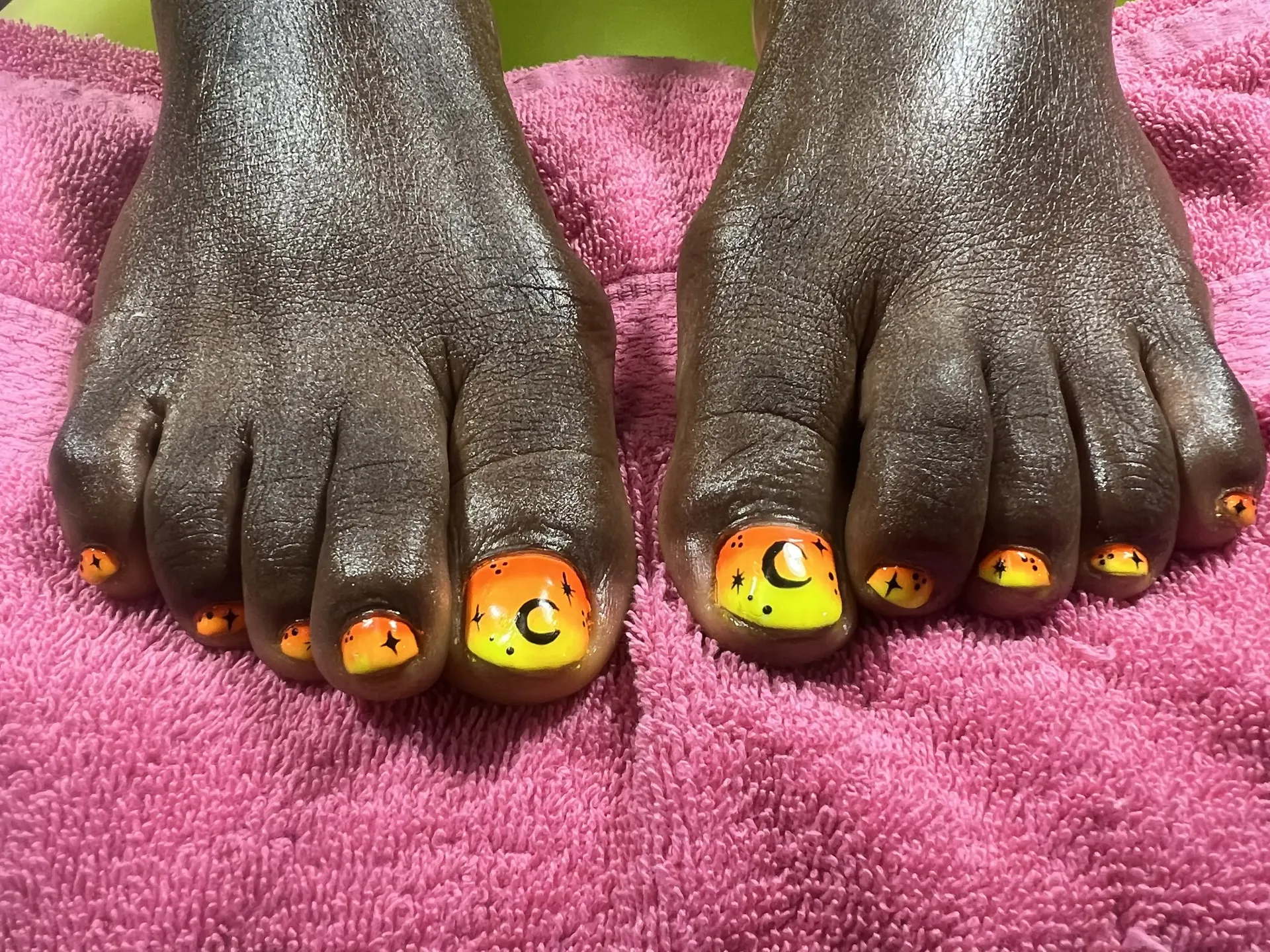 A pair of feet with yellow and orange nails on a pink towel.