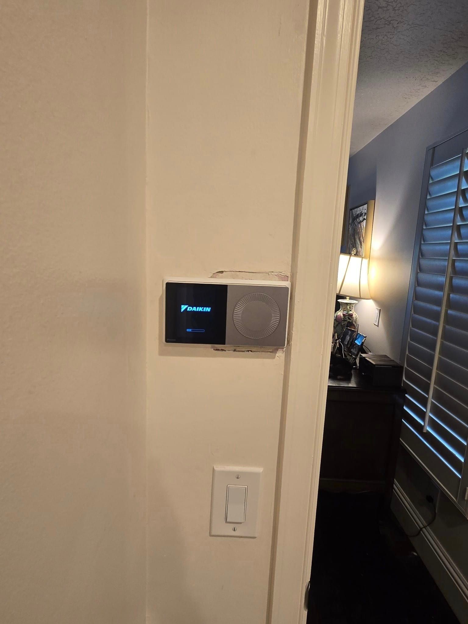 A thermostat is mounted on a wall next to a door in a bedroom.