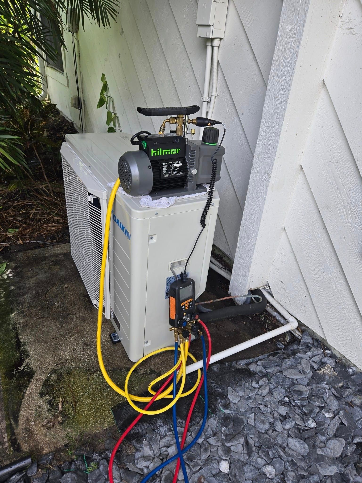 A vacuum pump is attached to an air conditioner outside of a building.