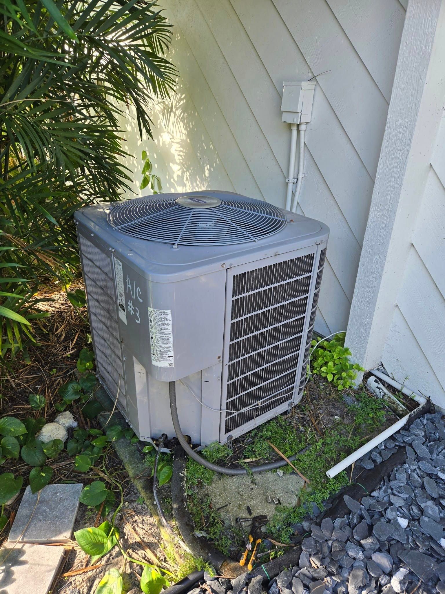 A gray air conditioner is sitting on the side of a house.