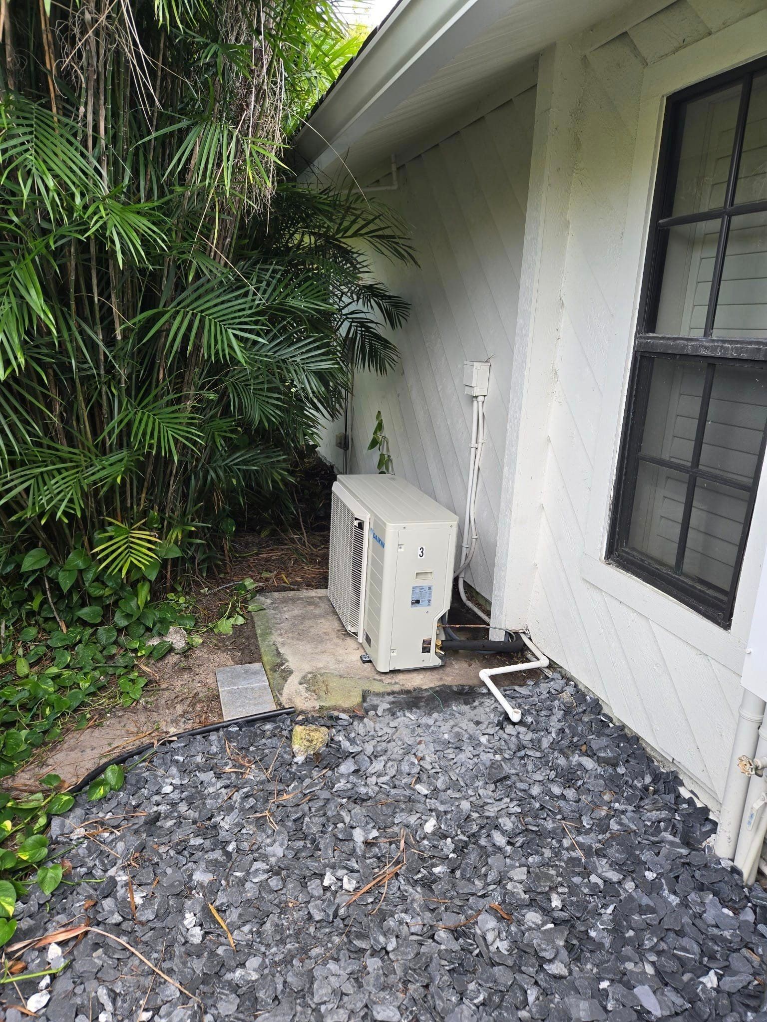An air conditioner is sitting on the side of a house next to a window.