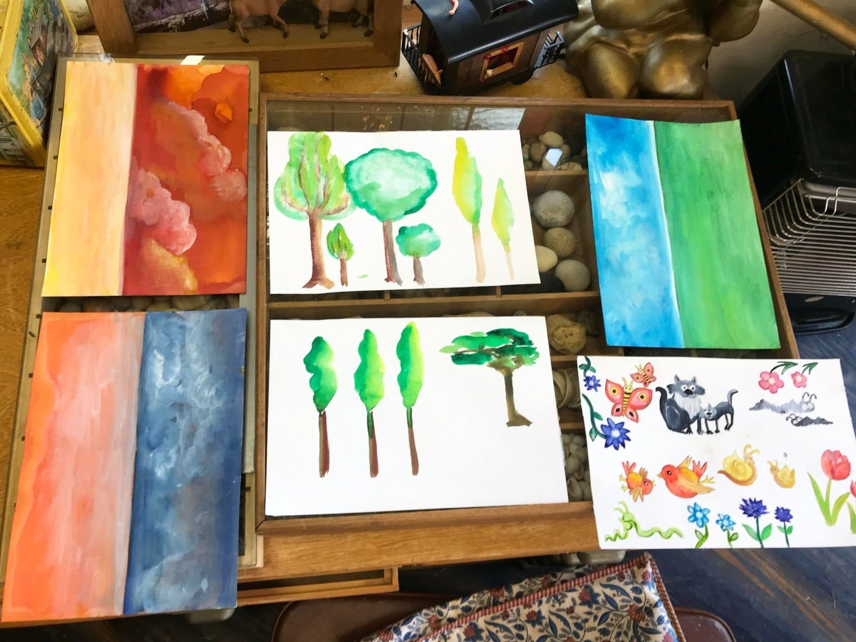 Aquarelkaarten met afbeeldingen van bomen, landschappen, bloemen en dieren, uitgestald op een houten tafel.