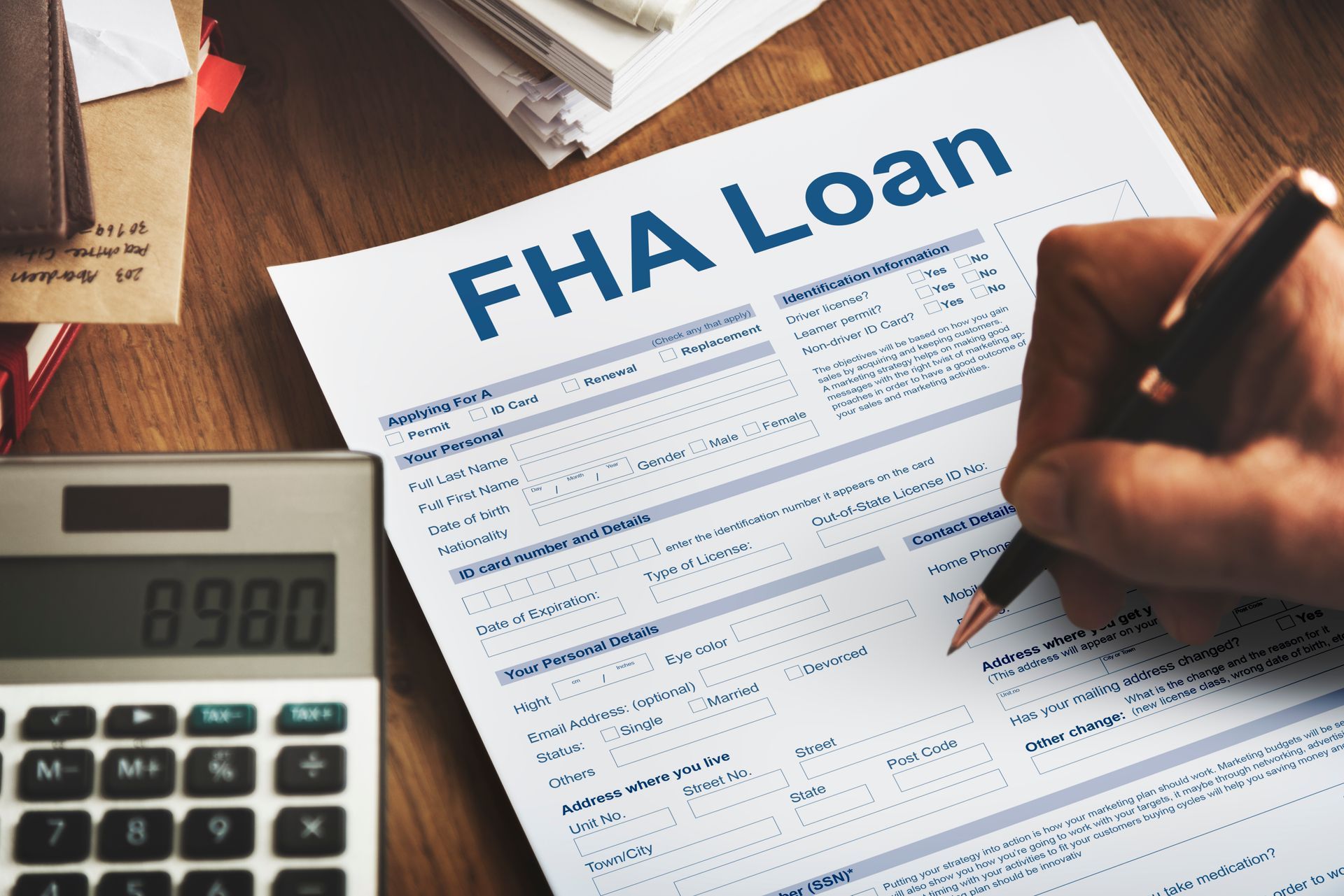 Person filling out an FHA loan form with a pen, calculator next to it.