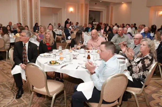 a large group of people are sitting at tables in a room applauding .