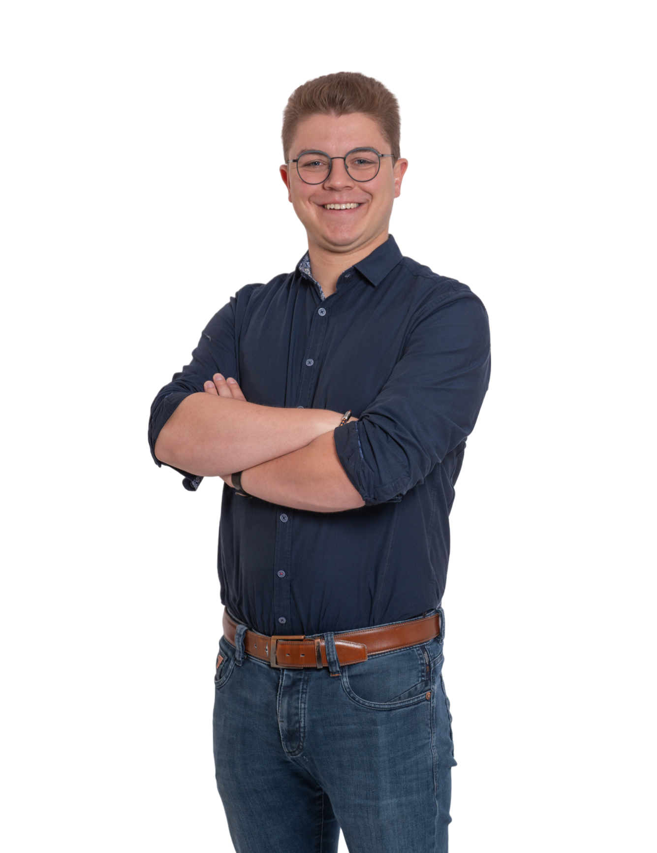 Lächelnde Person mit Brille, dunkelblauem Hemd und Jeans, die mit verschränkten Armen vor einem weißen Hintergrund steht