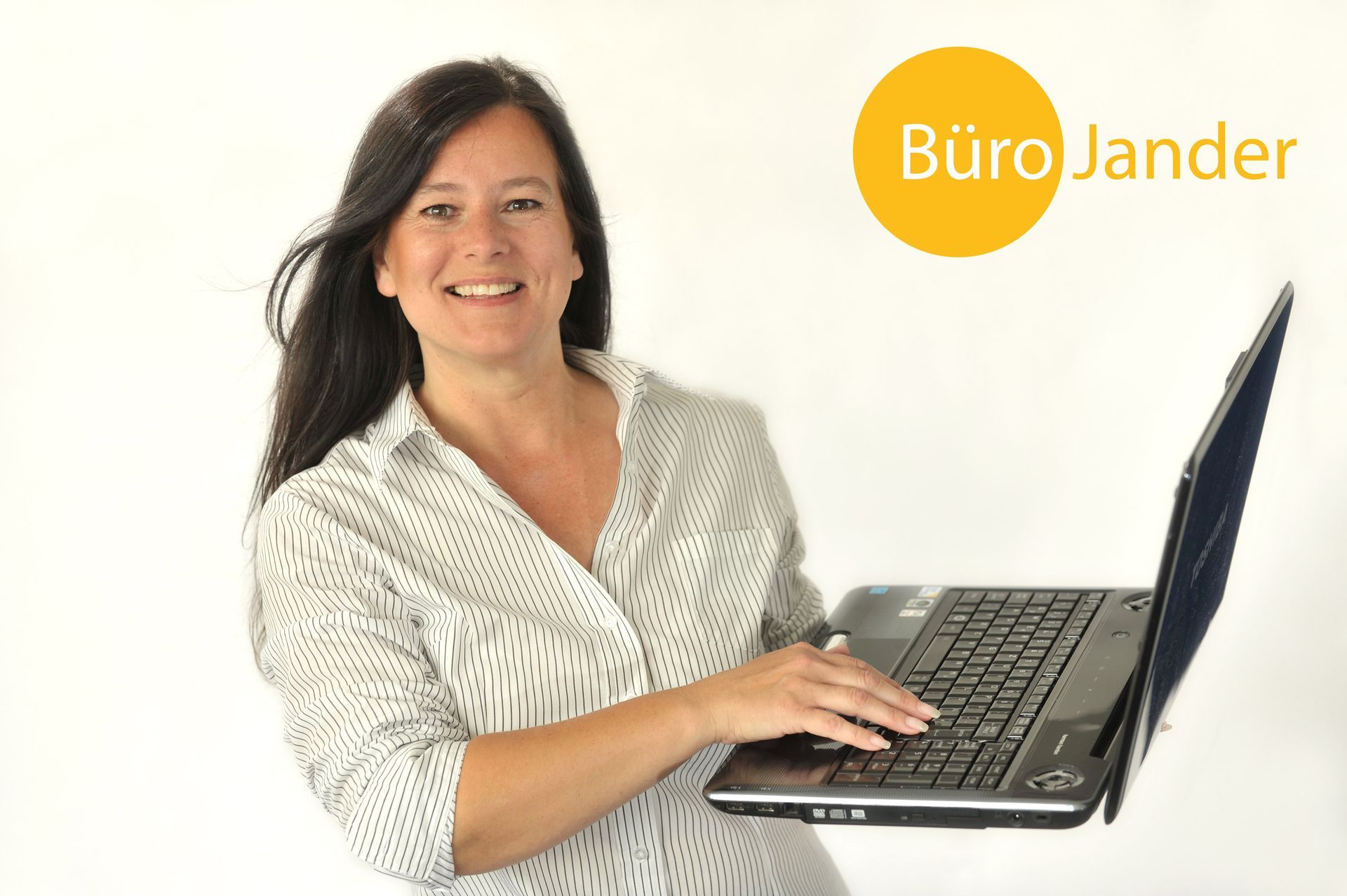 Frau in weißer Bluse lächelt, während sie auf einem Laptop mit gelbem „Büro Jander“-Logo tippt.
