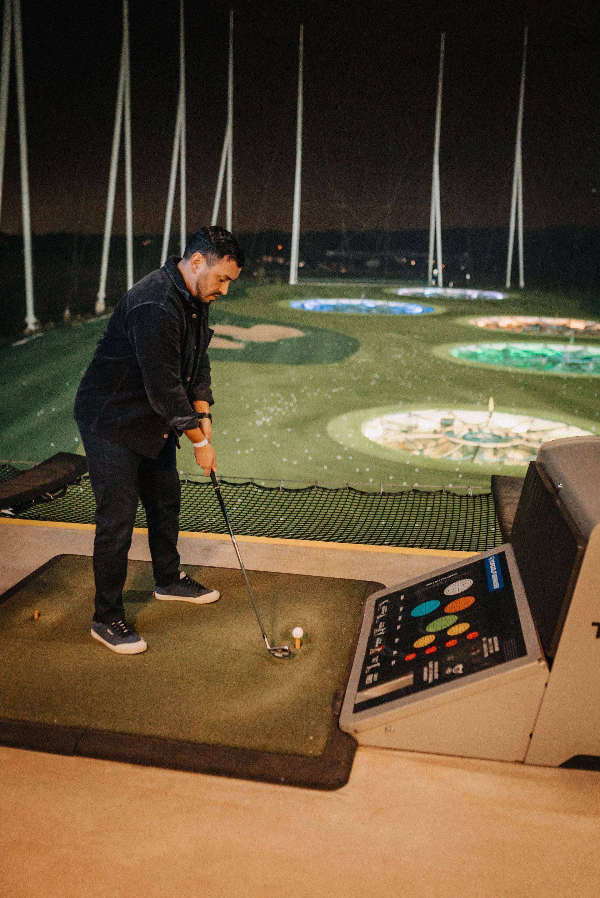 Ein Mann schwingt einen Golfschläger in einer Topgolfanlage und zielt unter Nachtbeleuchtung auf leuchtende Ziele.