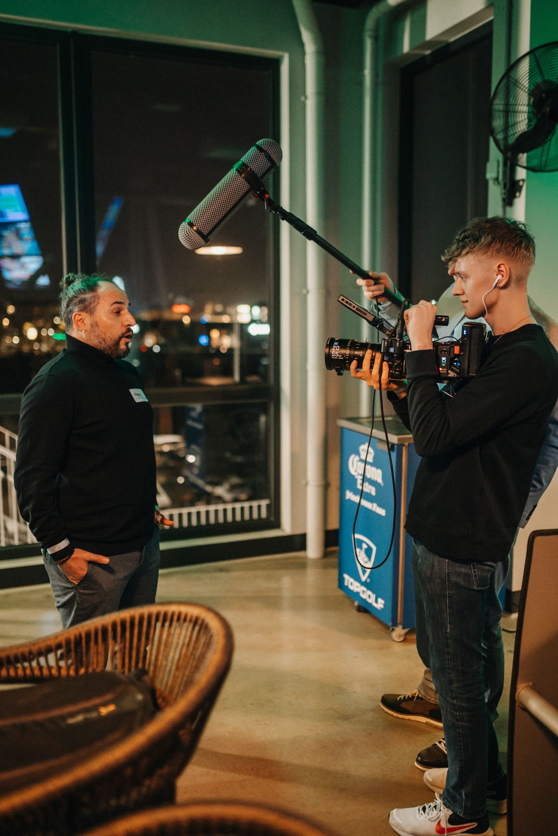 Ein Mann wird nachts in einem Veranstaltungsort interviewt und dabei von einer Person mit einer Kamera.