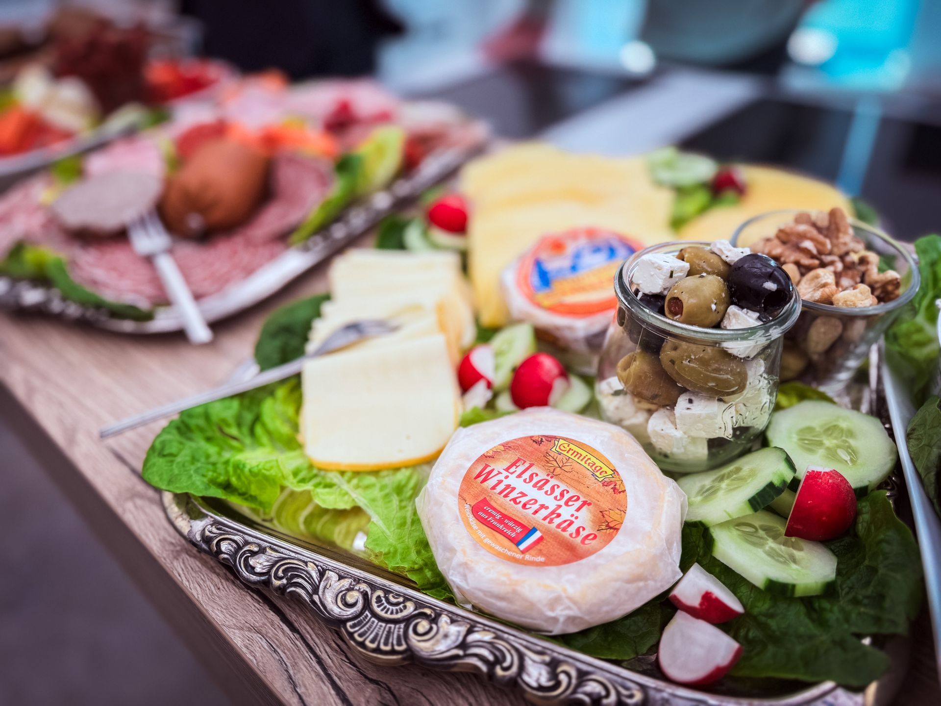 Nahaufnahme einer silbernen Platte mit verschiedenen Käsesorten, Oliven, Nüssen und Fleisch.
