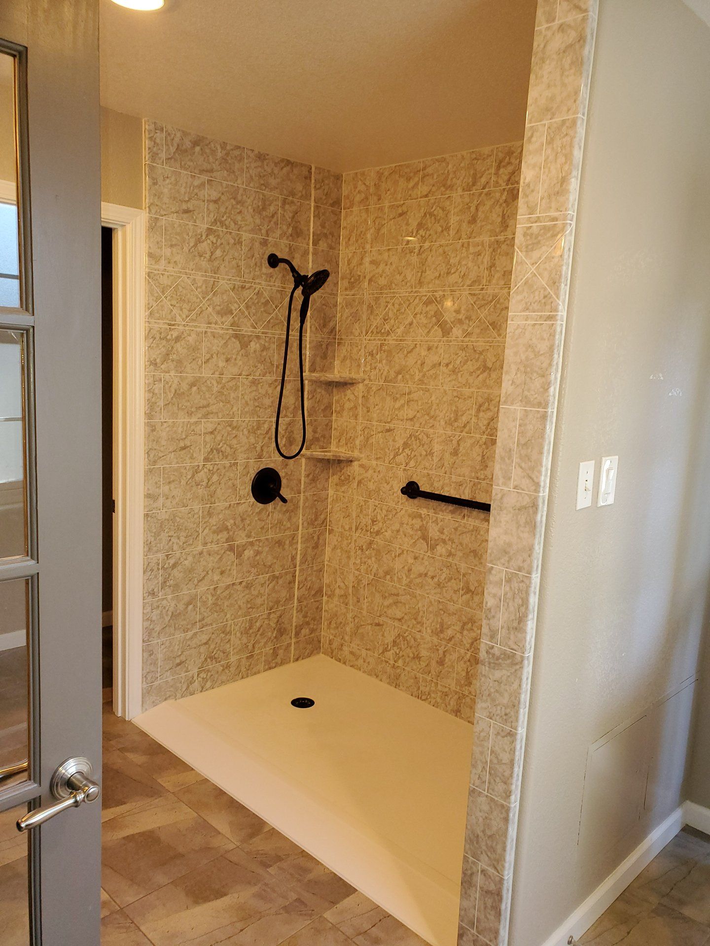 Walk-in shower with beige tile walls, white shower pan, and black shower fixtures
