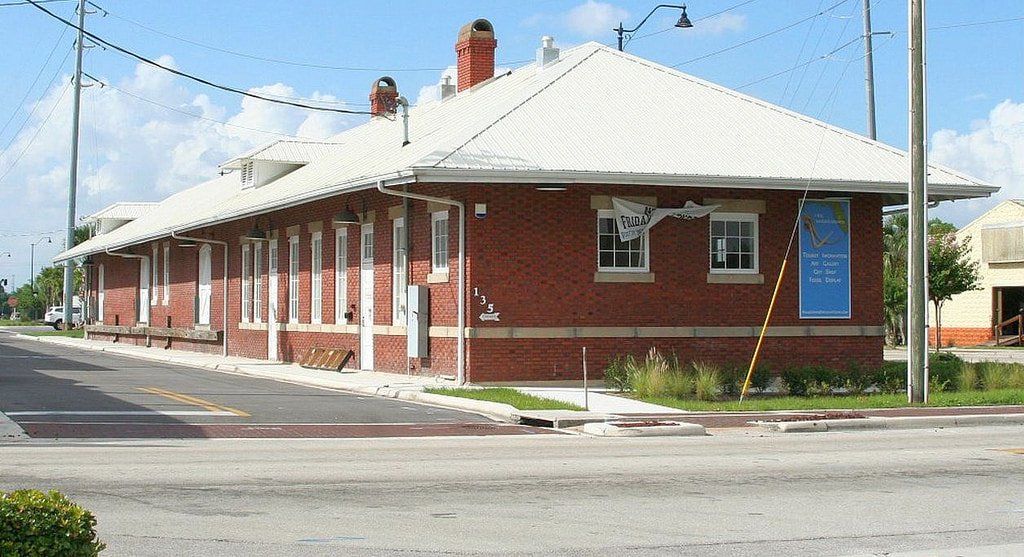 Red brick building with a white, angled roof. It sits on a street corner, with sidewalks and power lines visible.