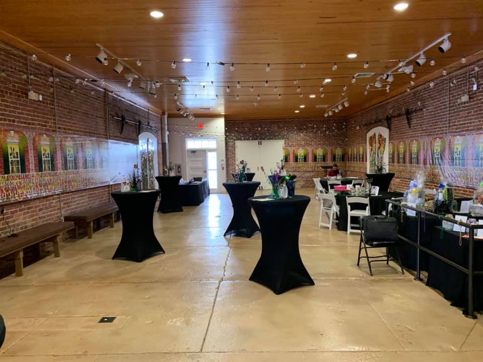 An event space with brick walls, a wooden ceiling, and several high-top tables covered in black cloth. Artwork lines the walls.
