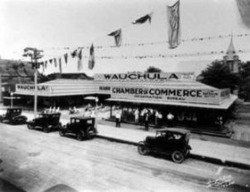 Wauchula Chamber of Commerce building with vintage cars parked out front, flags overhead, and a crowd of people gathered.