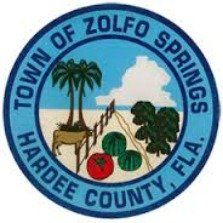 Seal of Zolfo Springs, Florida. Blue ring surrounds a scene of palm trees, an animal, crops, and a white cloud on a blue and beige background.