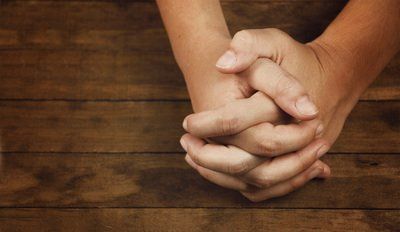 Two hands clasped together in prayer on a wooden surface.