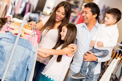 Family of four shopping for clothes in a clothing store, looking at hangers with smiling expressions.