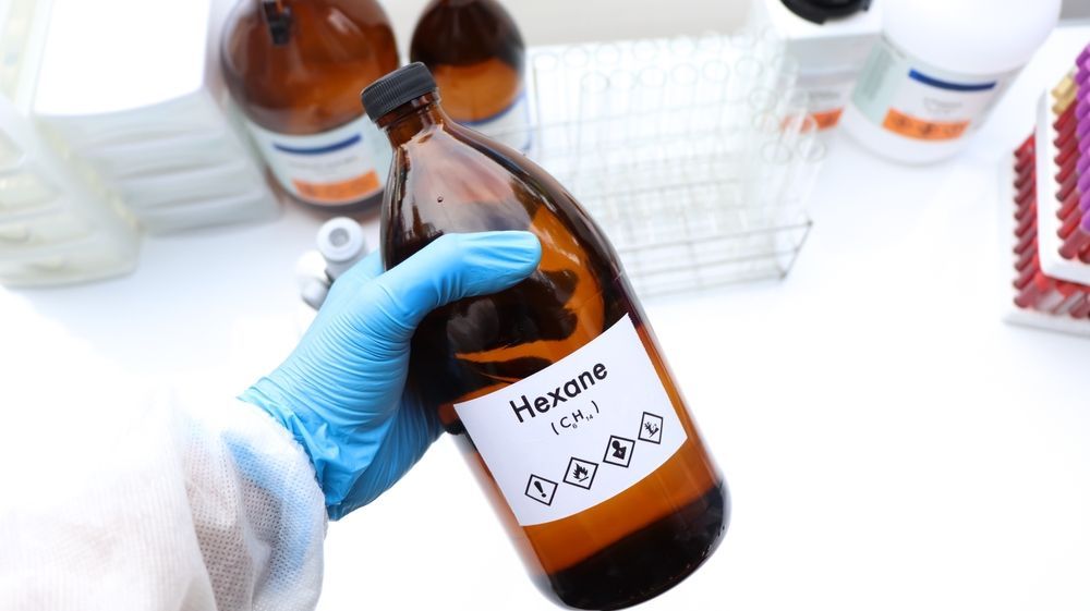 Gloved hand holding a brown bottle labeled “Toluene” in a lab setting