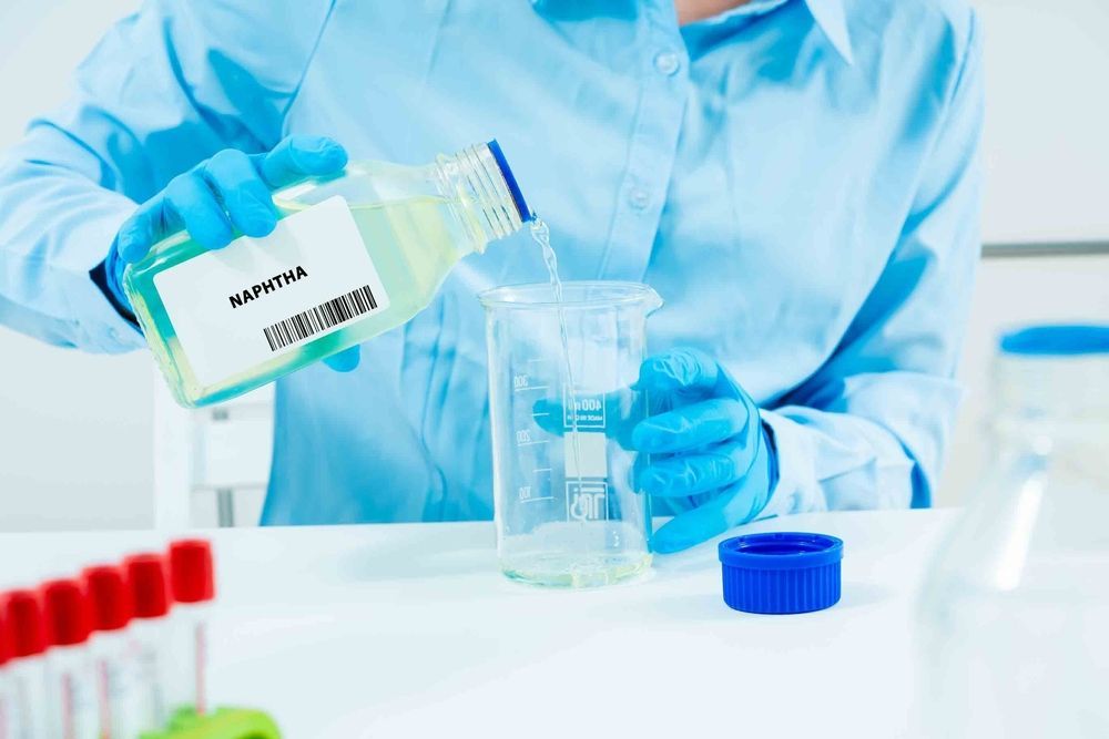 Person pouring liquid from a labeled bottle into a beaker in a lab setting