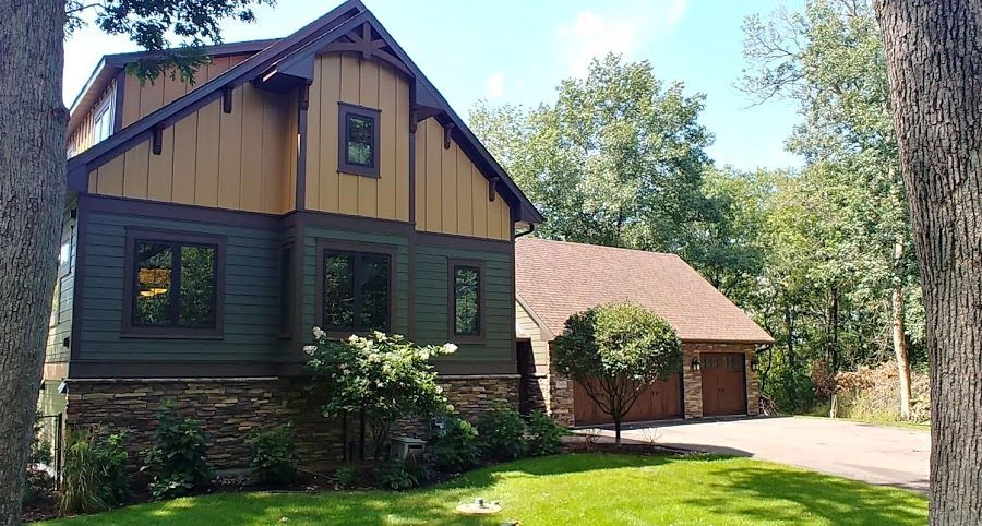 Two-story house with a brown and green exterior and a detached garage, set on a green lawn.