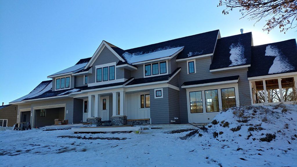 Large, two-story house with gray siding, snowy yard, and blue sky.