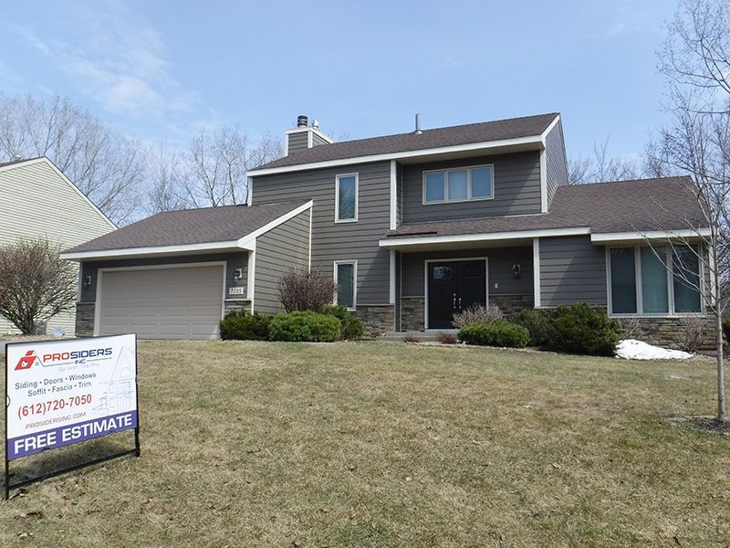 Two-story house with gray siding, brown roof, and a sign for 