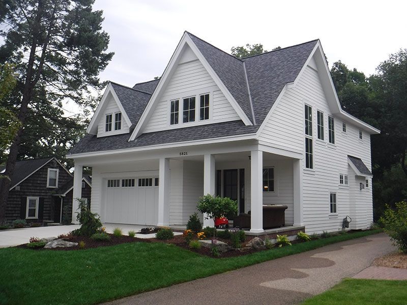 White two-story house with a gabled roof, garage, and porch. Lush green lawn and driveway in the foreground.