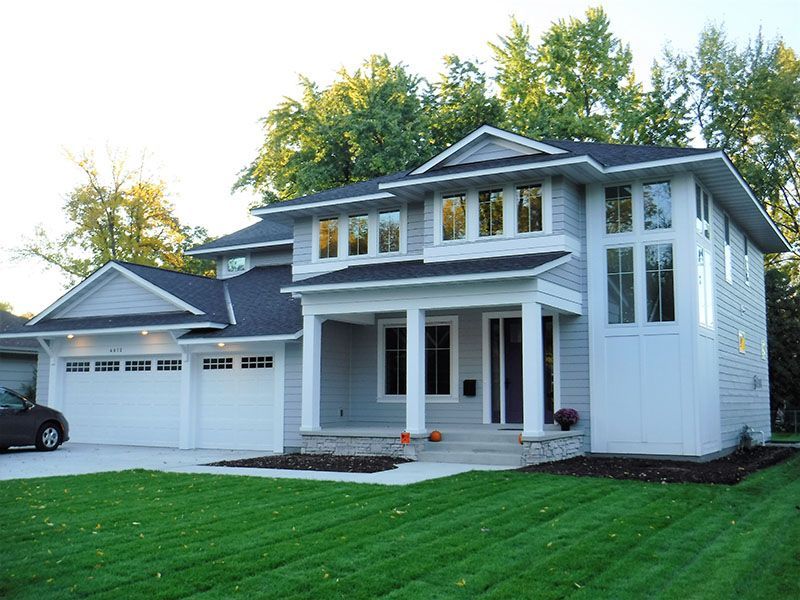 Two-story gray house with white trim, garage, front porch, and lush green lawn.