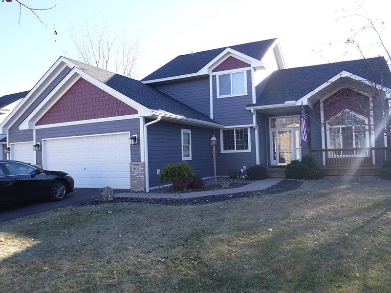 Two-story house with blue siding, a garage, and a curved walkway in a yard with sparse grass.