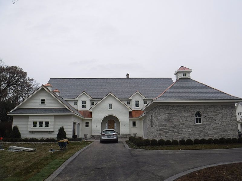 White building with dark roof, arched entrance, and stone addition; a car is parked in the driveway.