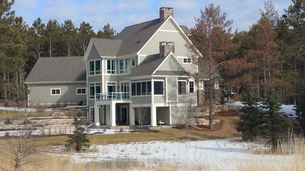 Two-story gray house with multiple windows and balconies, set in a snowy, wooded area.