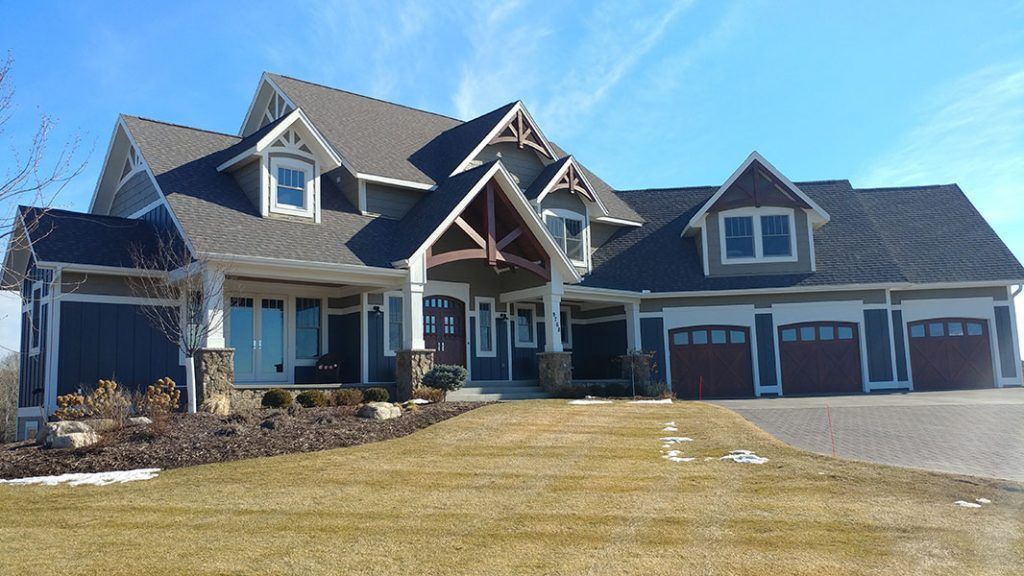 Large, two-story house with dark siding, brown roof, and three-car garage on a sunny day.