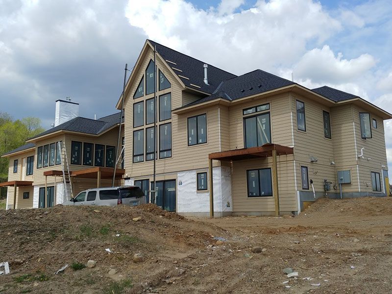 Under construction, two-story house with tan siding, black windows and roof, and a van parked in front.