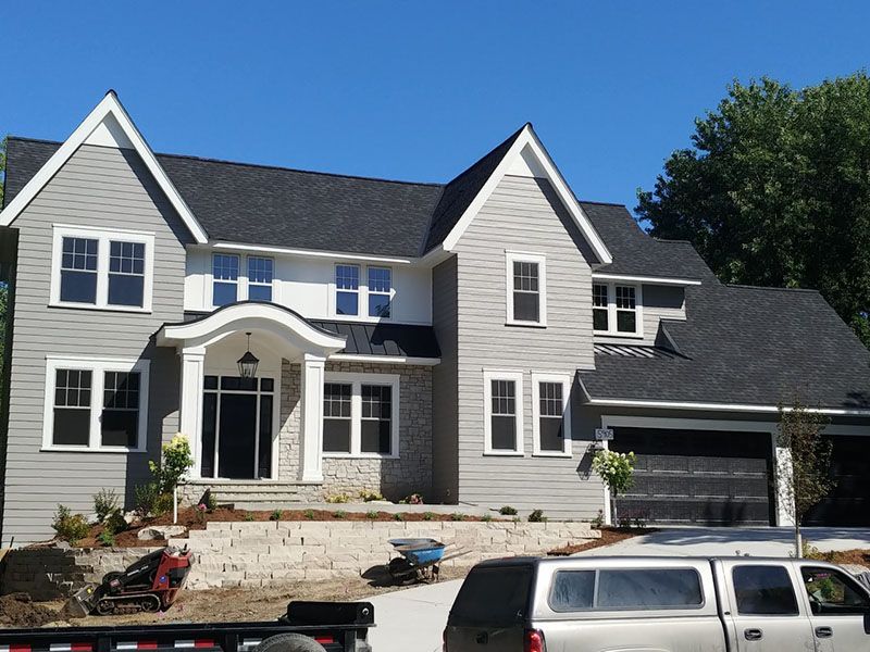 Two-story gray house with black roof, white trim, stone accents, and a garage; clear blue sky.