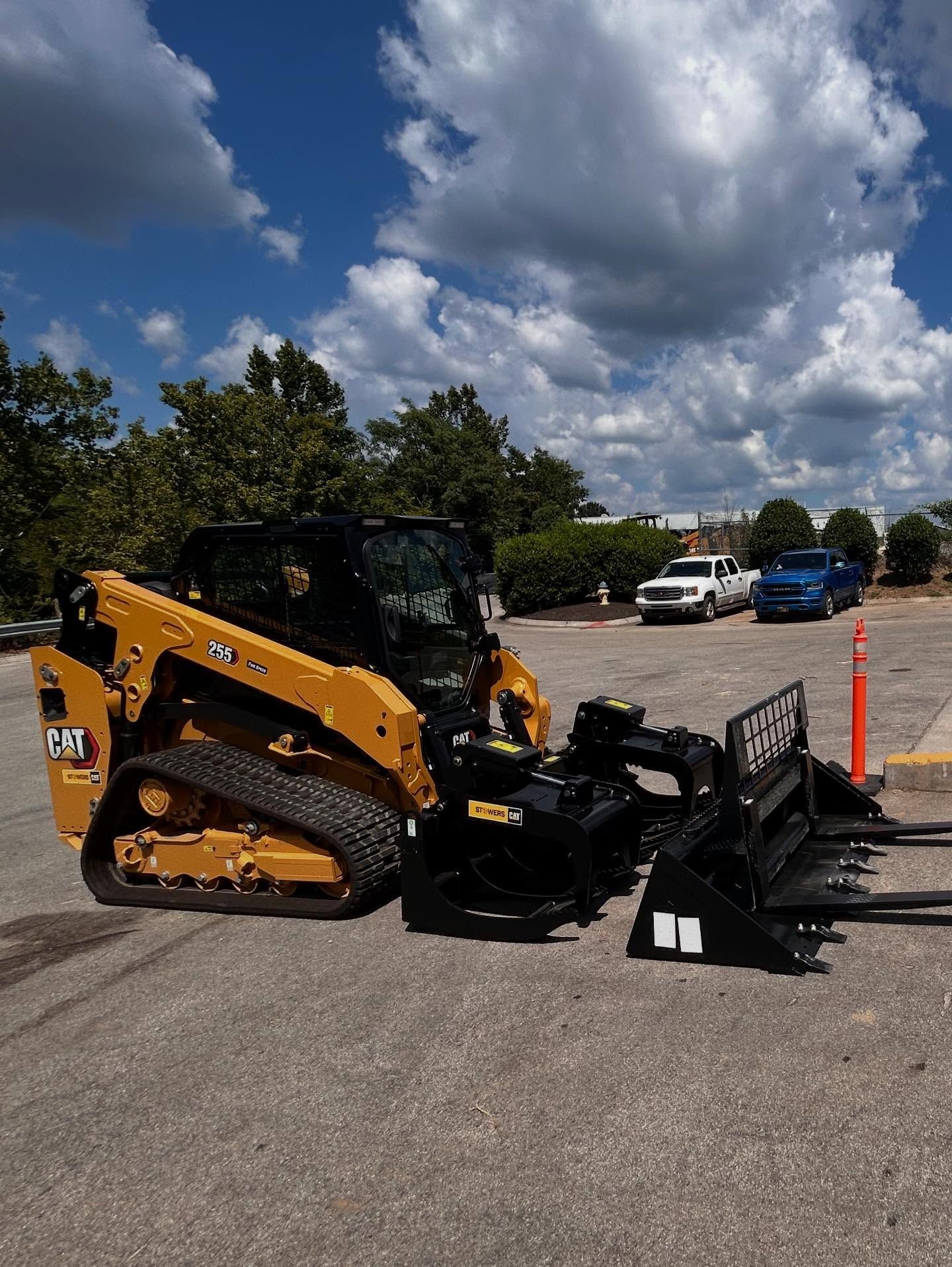 Yellow Caterpillar skid steer with black attachments parked on pavement, blue sky background.