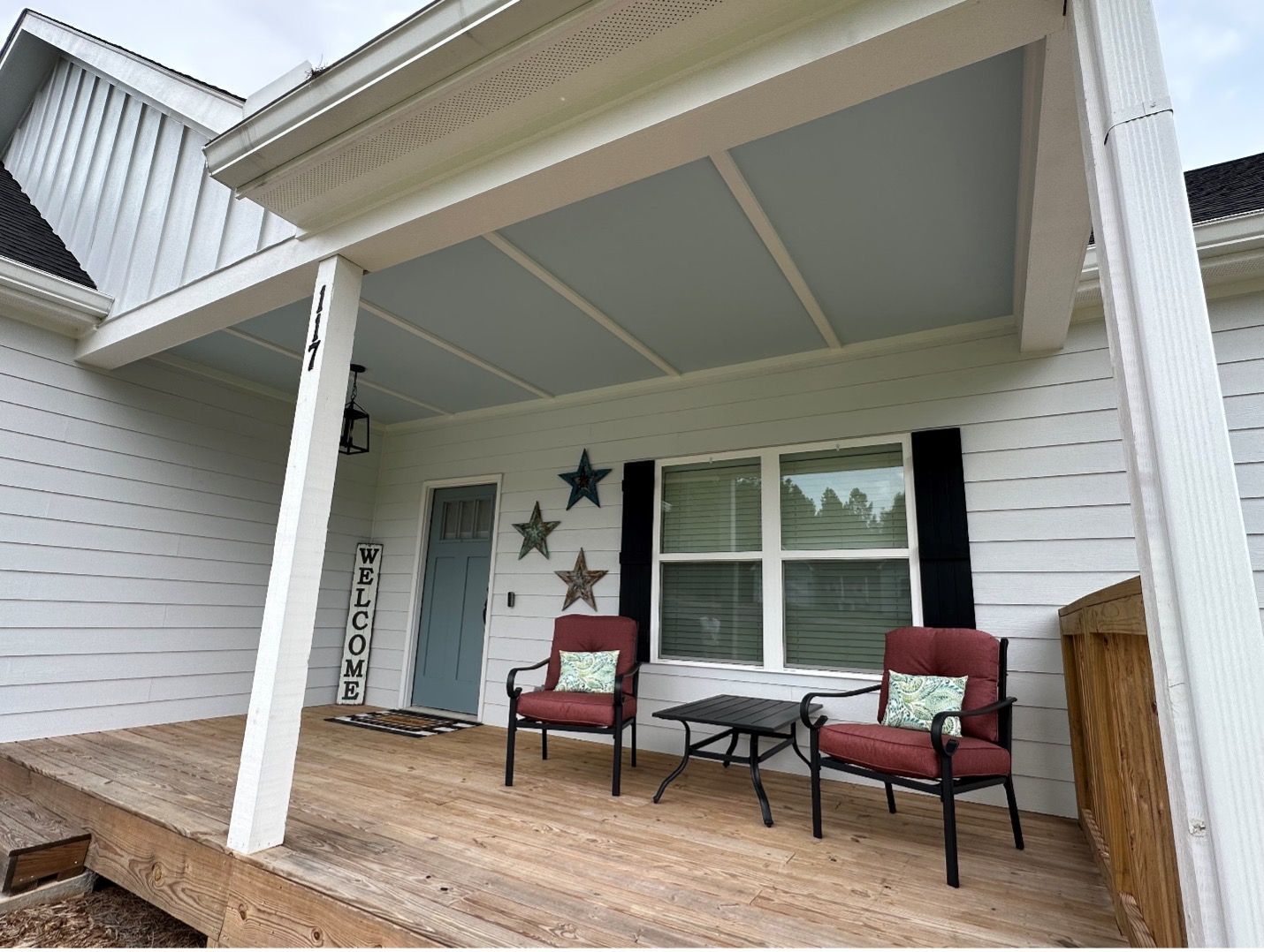 A porch with chairs and a table in front of a house.