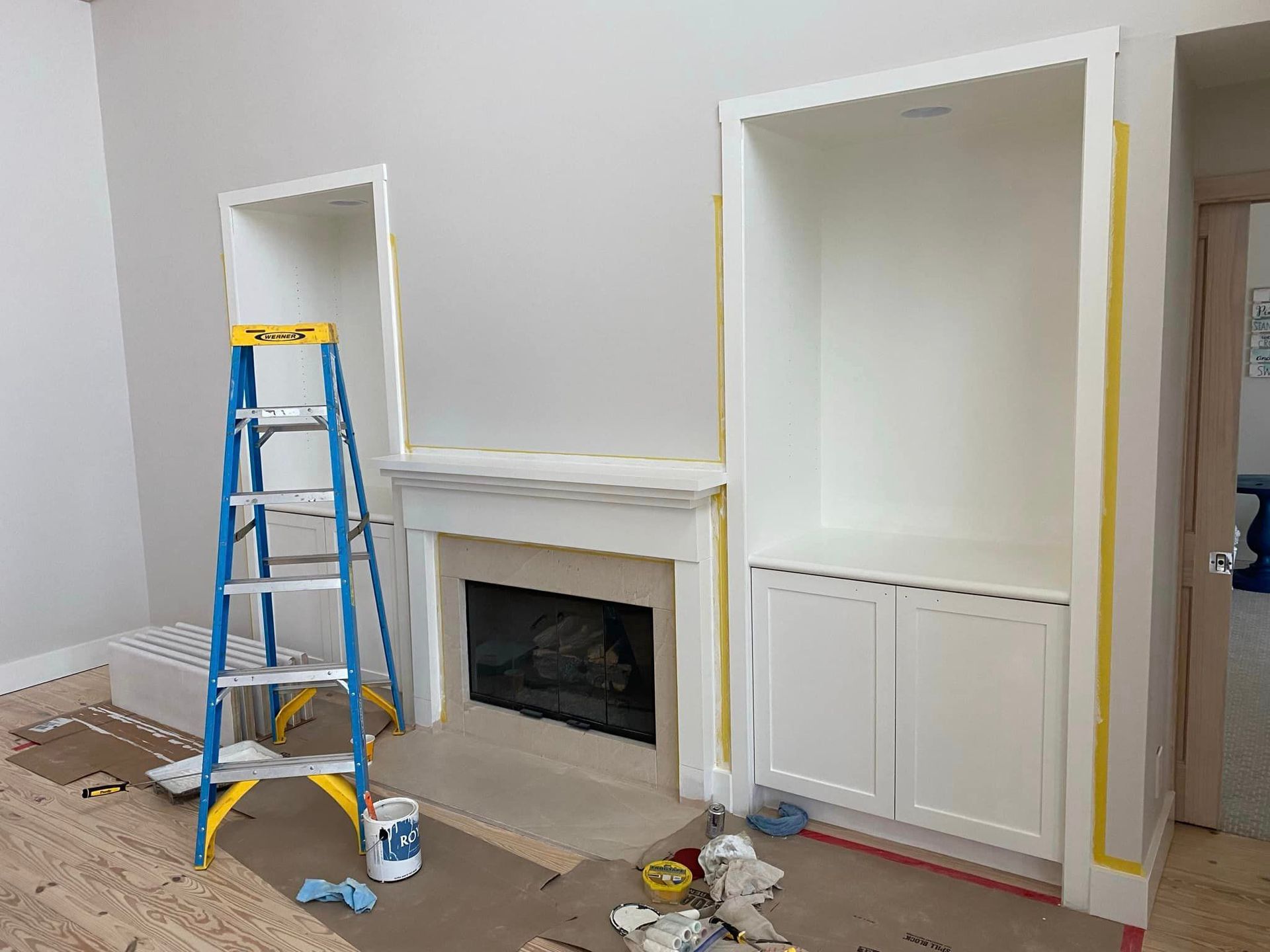 A living room is being painted with a ladder and a fireplace.