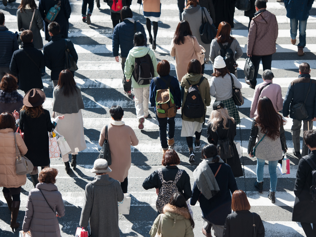 People crossing a busy city street at a crosswalk, viewed from above.