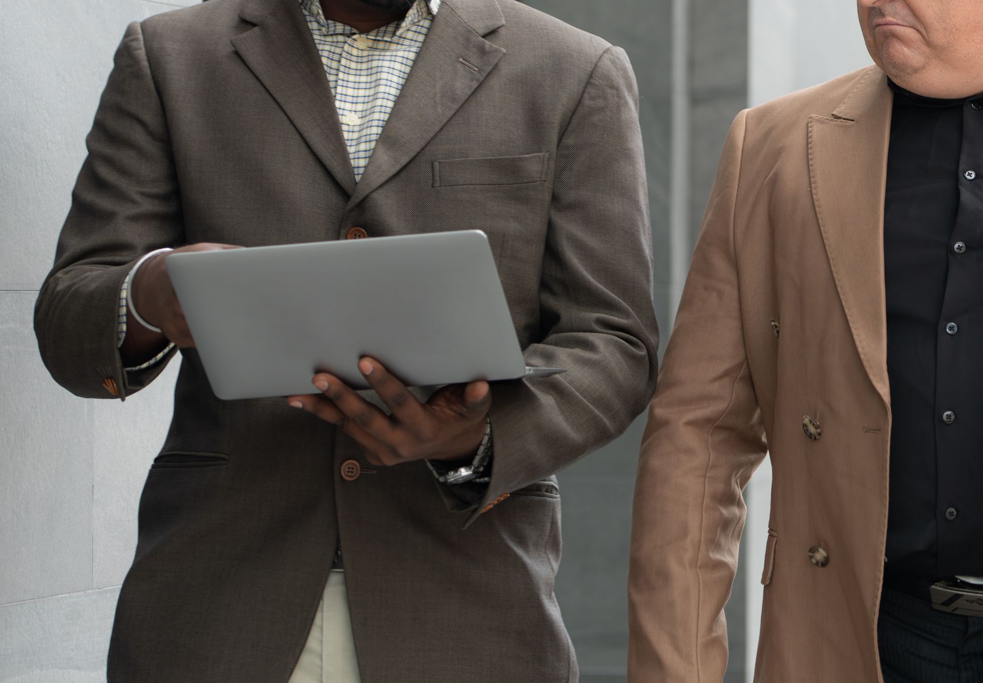 Two men in suits are standing next to each other and one is holding a tablet.