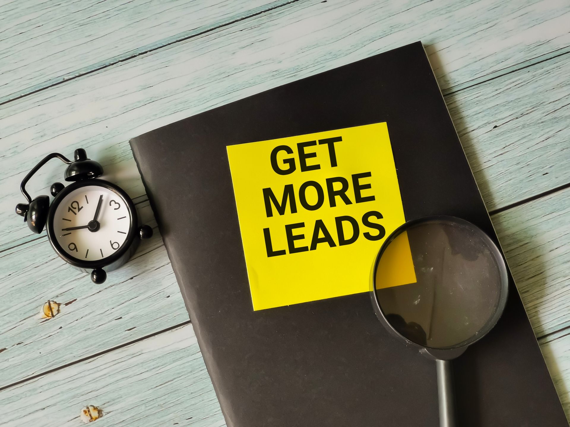 A black book with a yellow sticker that says `` get more leads '' next to an alarm clock and a magnifying glass.
