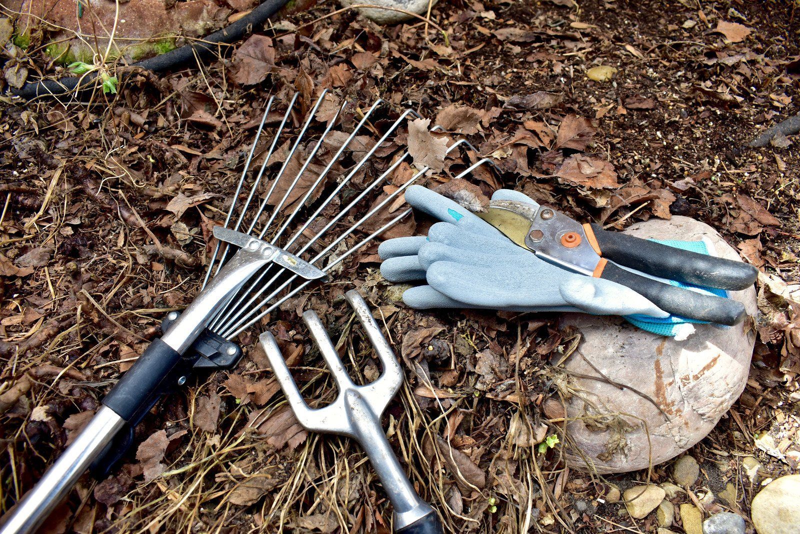 A pair of gloves and a rake are laying on the ground.