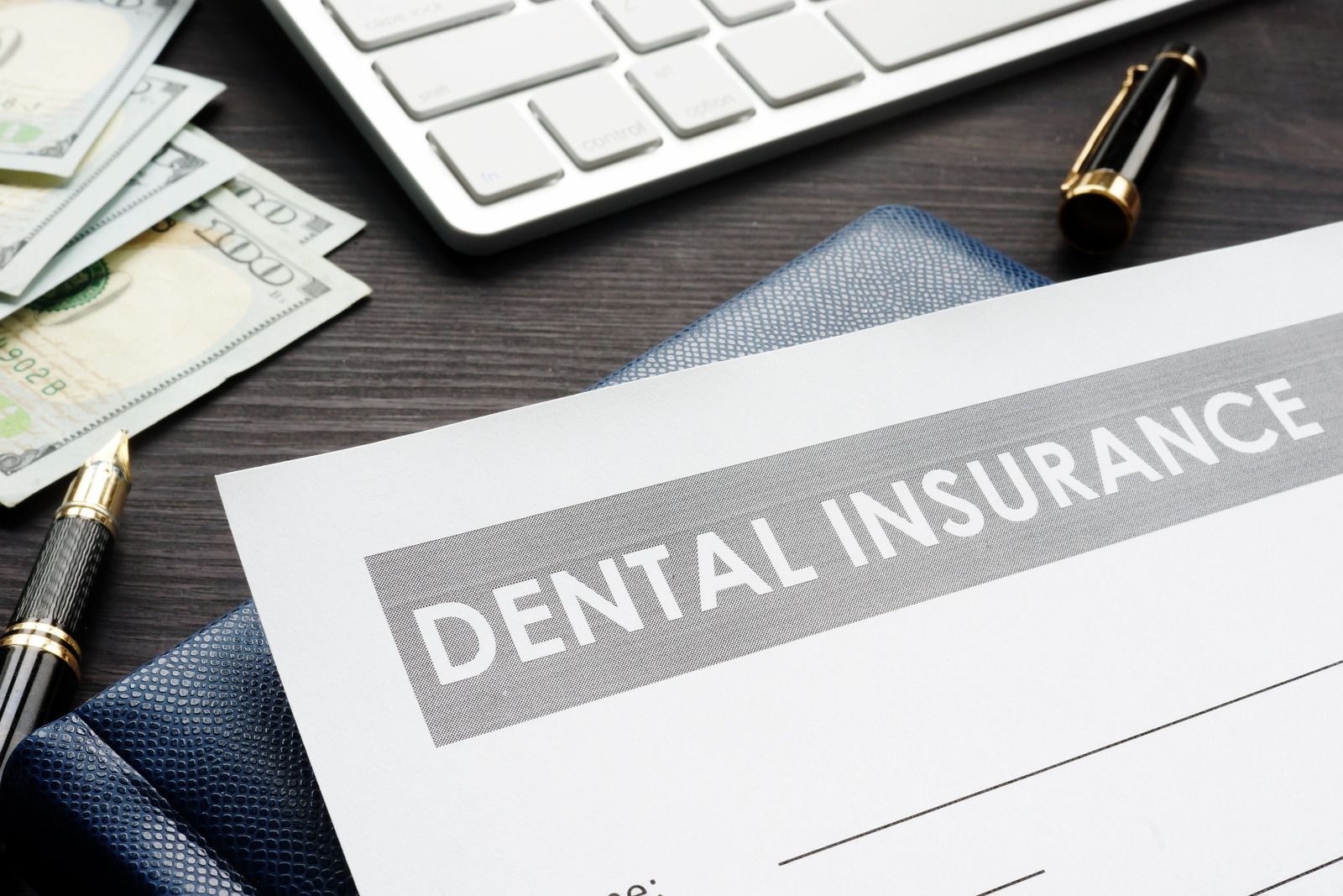 Dental insurance document on a desk with cash, pen, and keyboard.
