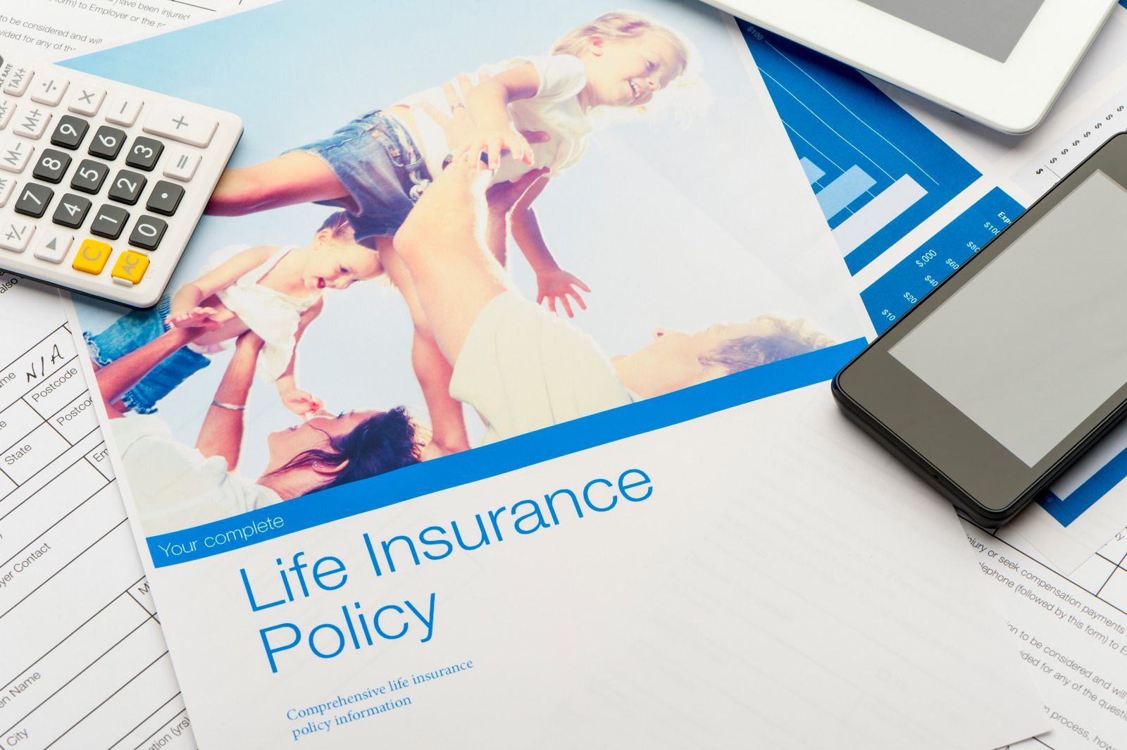 Life insurance policy papers on desk with calculator, tablet, and family photo