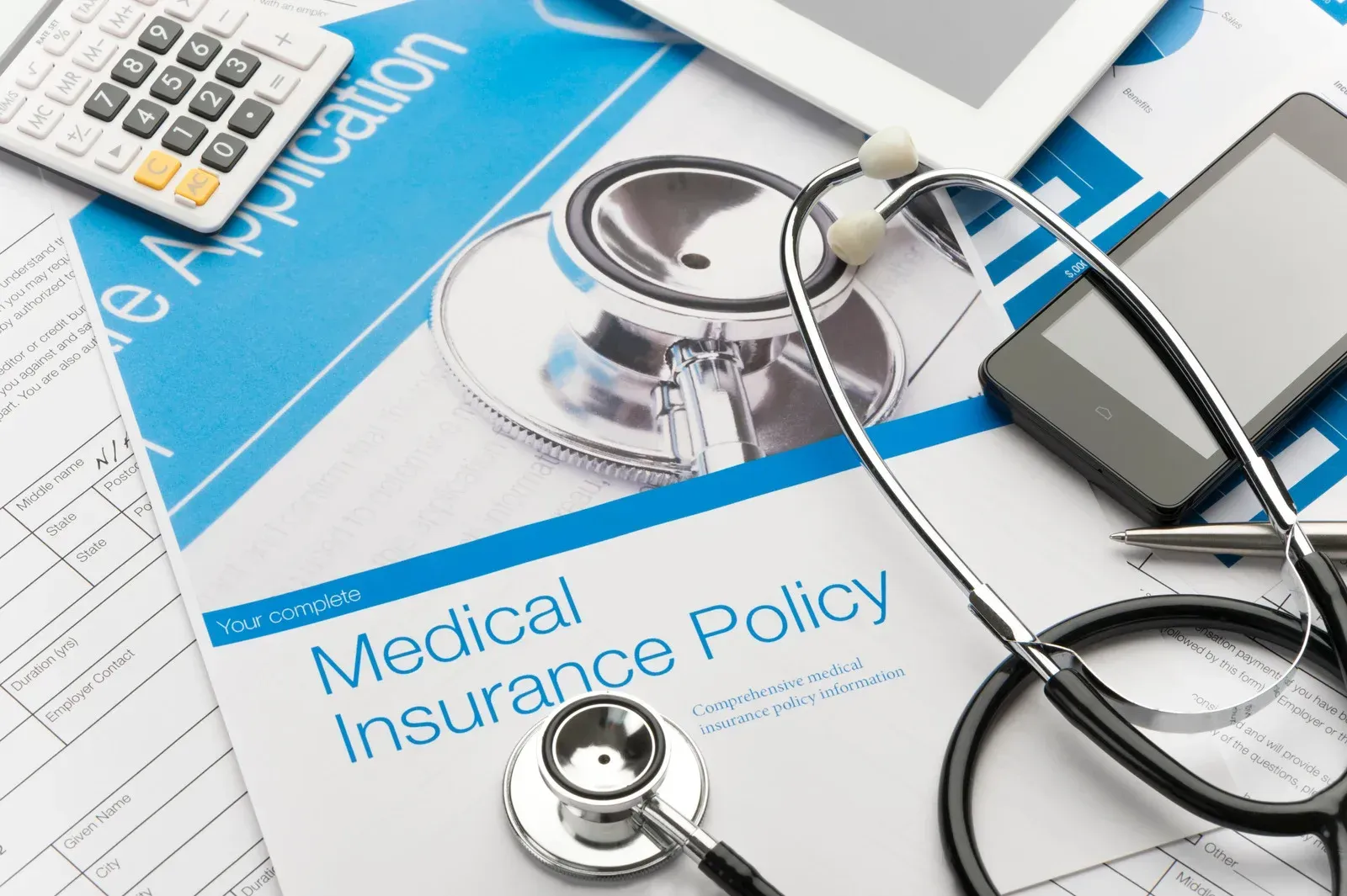 Medical insurance policy booklet with stethoscope, calculator, and pen on a blue desk