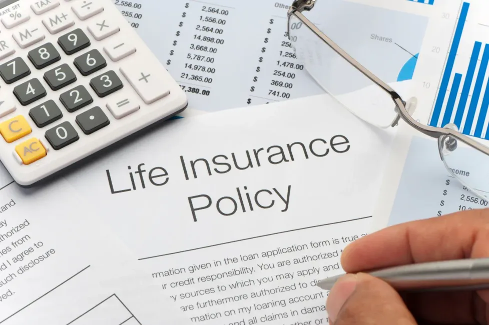 Life insurance policy document with calculator, charts, and a hand writing on paper