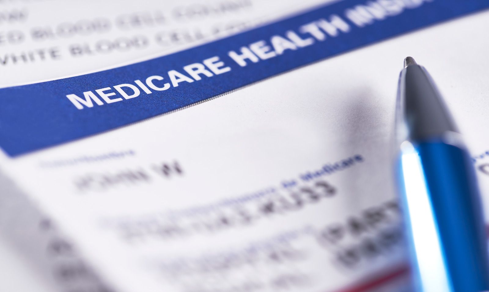 Blue pen on a Medicare health insurance card with blurred text in the background